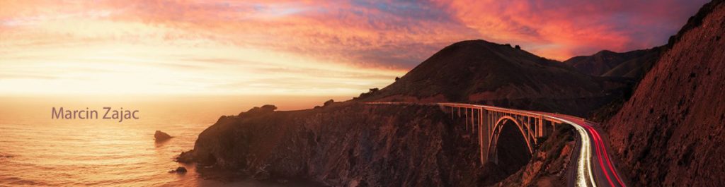 Bixby Bridge along California’s Highway 1 at sunset, with red and white light trails from cars and a vivid sky.