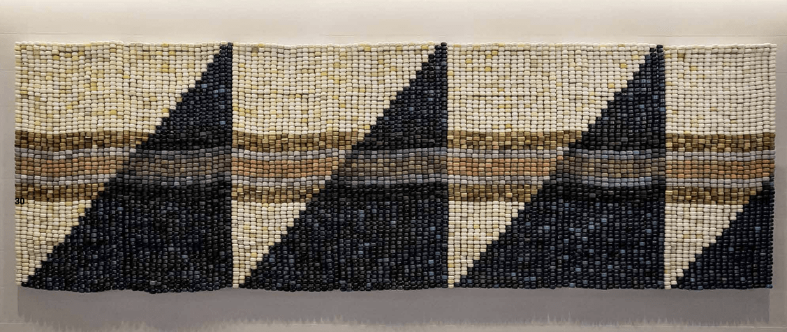 Large-scale beaded artwork by Ishi Glinsky of the Tohono O’odham Nation, created from cast adobe beads and skateboard wheels, loomed in the style of Indigenous regalia with geometric patterns in blue, cream, and earth tones.